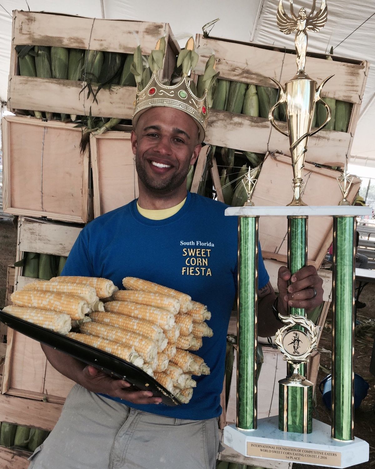 Yasir Salem wearing a crown, holding a tray of corn cobs and a tall trophy